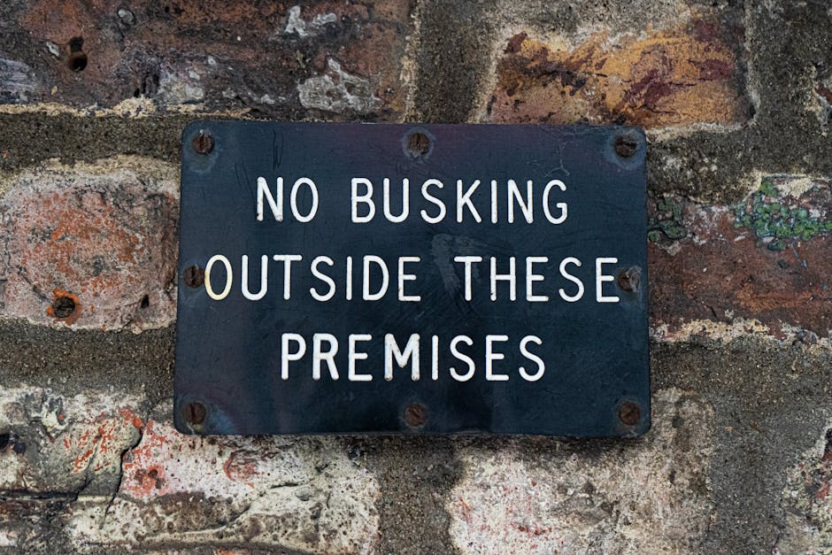A pair of red metal signage panels mounted on a black pole outside a property, indicating a designated alcohol-free zone as part of street-loading restrictions in Haringey, London. Each sign features