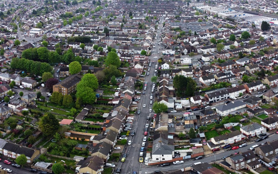 An aerial view of a residential neighbourhood in Enfield, showcasing rows of terraced houses with small front gardens and parked cars lining the streets. The street scene includes a variety of househo